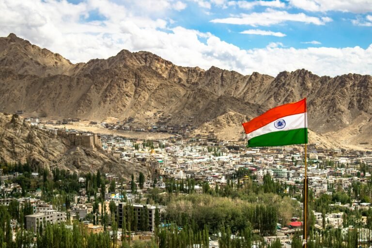 View of Leh city with the Indian flag against majestic mountains under a vibrant sky.